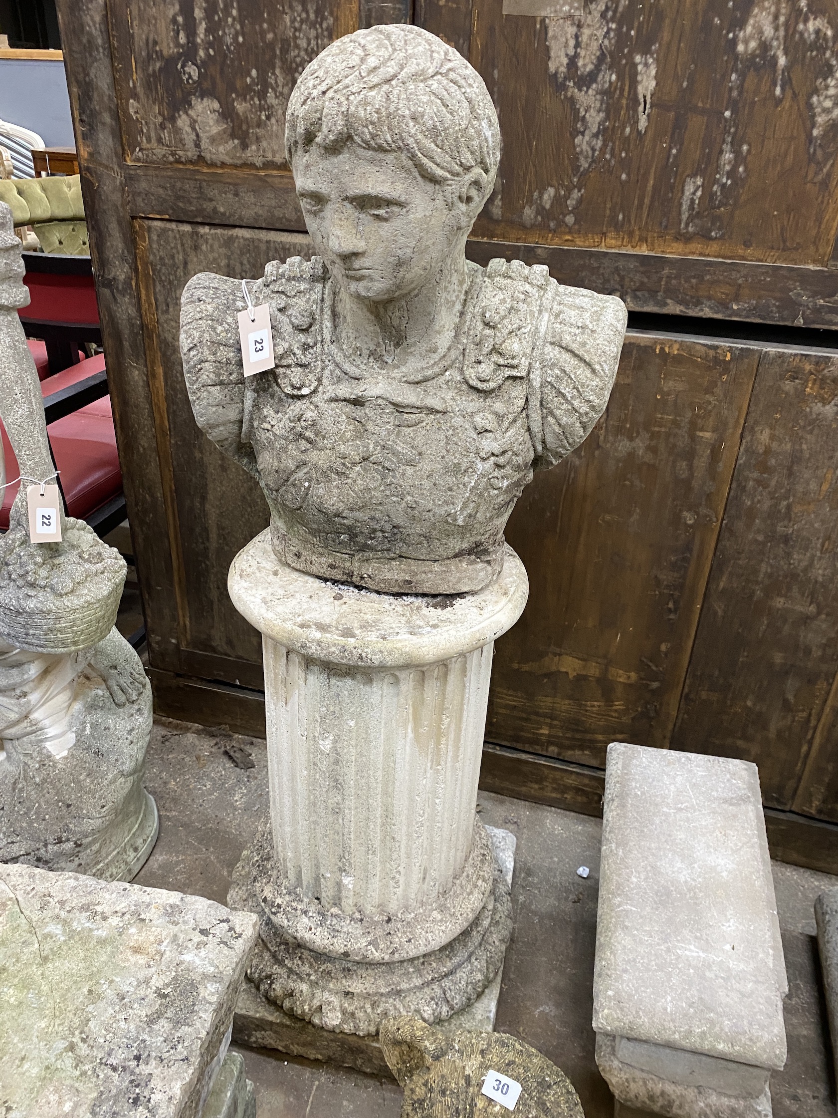 A reconstituted stone bust of a Roman warrior, on circular fluted plinth, height 123cm